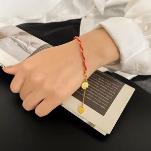 Detail of red braided rope bracelet with golden Xi character charm and adjustable chain