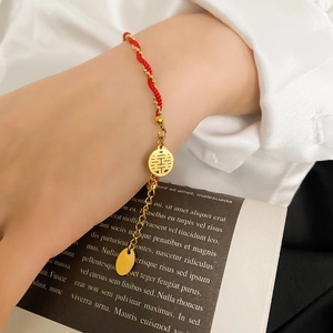 Detail of red braided bracelet with gold Xi character charm and bead accents
