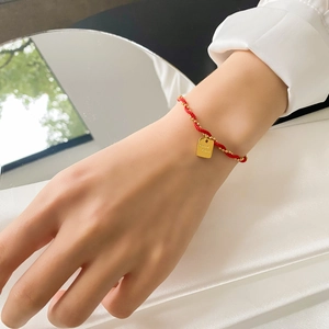Detail of red braided lucky bracelet with golden beads and Good Luck square charm