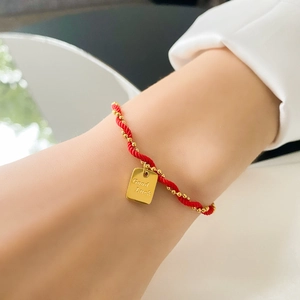 Detail of red braided cord bracelet with gold beads and Good Luck engraved square tag