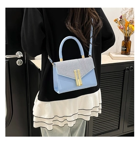 Detailed view of light blue leather handbag with gold accents worn by a model