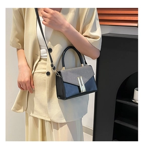 Detail of the gray fabric flap and gold vertical metal buckle on the black shoulder bag
