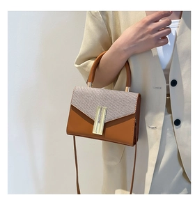 Detail of a brown woven contrast shoulder bag with a gold H-shaped buckle worn by a model