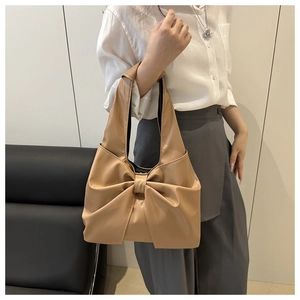Detail of a khaki shoulder bag featuring a large decorative bow and polished leather texture
