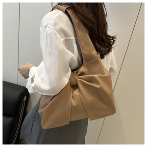 Detail view of the light brown shoulder bag with a large decorative bow and soft leather texture