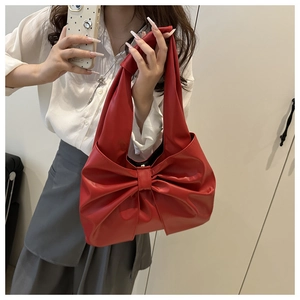 Detail of red faux leather handbag featuring a large decorative bow and smooth texture