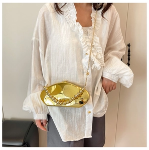 Dettaglio della pochette dorata a forma di pietra con manico di perle e catenina