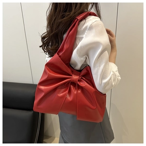 Fashionable red bow-shaped tote bag with pleated leather texture shown on shoulder