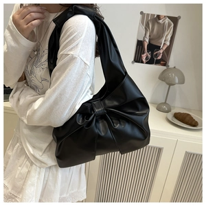 Close-up of a black matte leather bow-shaped shoulder bag on a female model