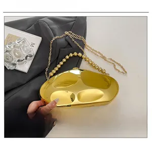 Dettaglio di una pochette dorata a forma di pietra con manico a perle e catena fine