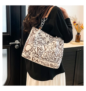 Detail of white canvas tote bag with brown graffiti prints and chain leather strap