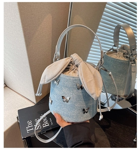 Detailed view of denim bucket bag with silver butterfly charms and large fabric bow