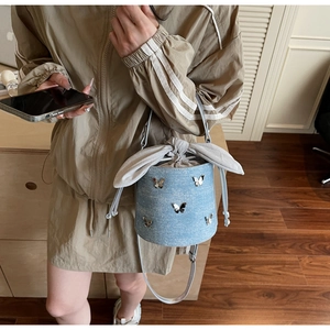 Detail of light blue denim bucket bag with silver butterfly charms and drawstring bow