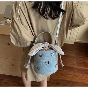Detail view of denim bucket bag with silver butterfly charms and drawstring closure