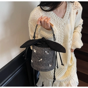 Detail of a denim bucket bag with silver butterfly charms and a black bow closure