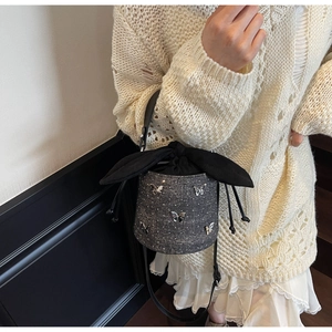 Detail of dark gray bucket bag with silver butterfly charms and silk ribbon closure