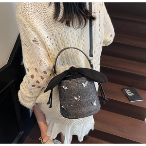 Detail of black sequined bucket bag with silver butterfly metal charms on stairs