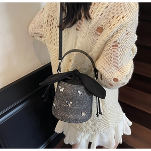 Detail showing dark denim bucket bag with silver butterfly accents and silk bow closure