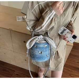 Detailed shot of washed blue denim bucket bag with silver butterfly charms and fabric bow