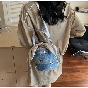 Detail of denim bucket bag with silver butterfly charms and bunny ear drawstring closure