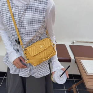 Yellow woven crossbody bag with golden flower buckle and wave flap shown on model