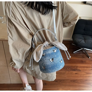 Blue denim bucket bag with silver butterfly charms and drawstring bow closure detail