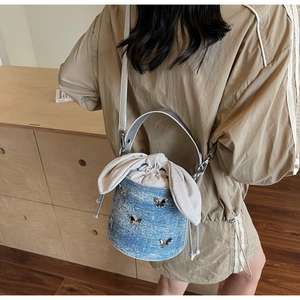 Detail of denim bucket bag with silver butterfly charms and drawstring closure