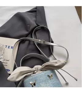 Detail of denim bucket bag showing adjustable strap, butterfly charm, and rhinestone accents