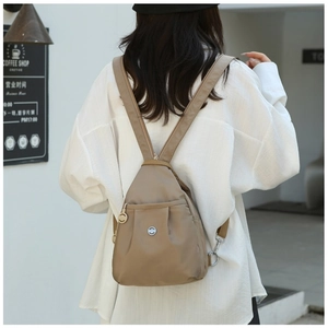 Close-up of a mini brown Oxford fabric backpack worn by a model in a casual setting