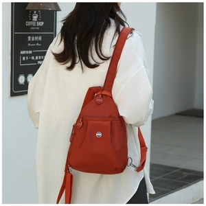 Detail of brick red nylon mini backpack on model showing strap texture and side D-ring