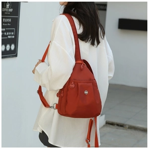 Close-up of a mini rust-red oxford cloth backpack on model in urban street setting
