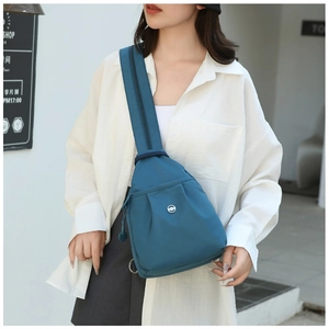 Blue oxford fabric sling bag worn by a model in a stylish urban street setting