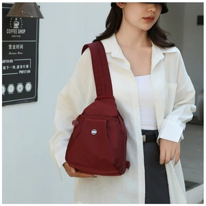 Close-up of burgundy nylon chest bag with adjustable strap and circular logo detail