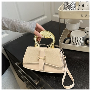 Macro shot of stylish square bag featuring a gold sculptural handle and woven texture