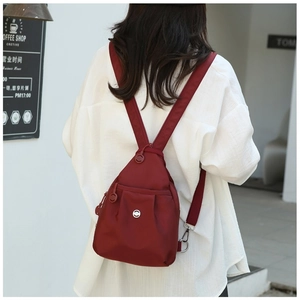 Lifestyle view of a stylish burgundy oxford cloth backpack styled with a white shirt outfit