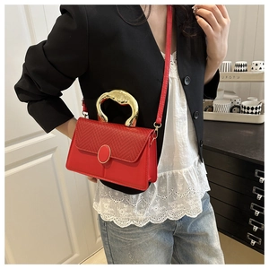 Detail of red crossbody bag featuring woven flap texture and unique wavy gold handle
