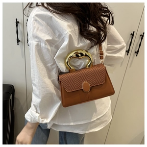 Detail of brown leather handbag with woven flap and polished gold sculptural handle