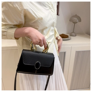 Detail of minimalist black crossbody bag with textured leather and unique gold metal handle