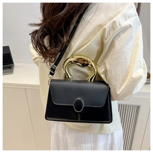 Detail of black crossbody bag with golden sculptural handle and mixed leather textures