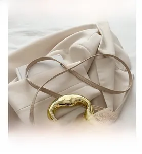 Detail of beige textured handbag with sculptural gold metal handle and slim shoulder strap