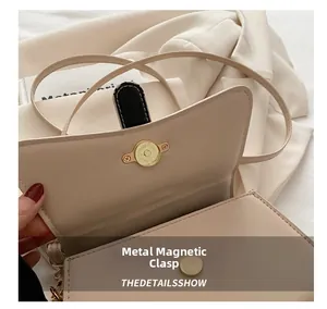Close-up of the elegant golden magnetic snap closure on a beige square crossbody bag
