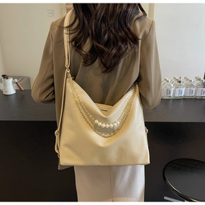 Detail of off-white leather tote bag with elegant gold chain and pearl strap decoration