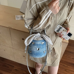 Blue denim bucket bag with metal butterfly and bow drawstring worn by a model