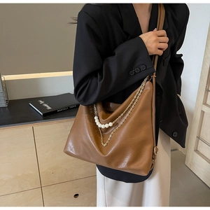 Detail of a large brown leather tote bag with elegant pearl and gold chain accents