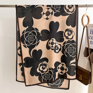 Detail of camellia flower print on beige scarf draped over a wooden hanger