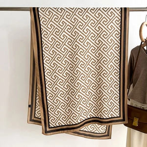 Detail of brown Greek key pattern scarf hanging on a metal rack with soft draping fabric