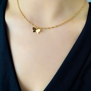 Gros plan d'un collier pendentif papillon doré porté sur la clavicule avec chaîne