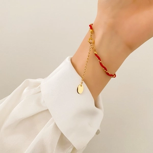 Detail of red braided lucky charm bracelet with gold chain and circular metal tag on wrist
