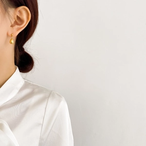 Close-up of elegant gold teardrop earrings worn by a model in a minimalist setting