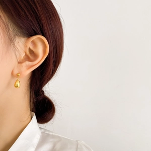 Detailed close-up of a high-polished golden teardrop earring worn on a model's ear lobe